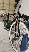 View of lightweight black bicycle frame with no seat or pedals, lightweight carbon fork, and front wheel with white sidewall tire attached.