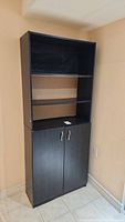 Full view of closed black wooden bookcase showing four shelves and two doors with handles.