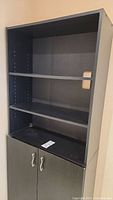 Front view of black bookcase with three visible shelves and two cabinet doors below.