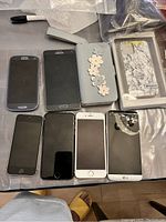 Front view of six smartphones and two phone cases on table showing screen side and case designs