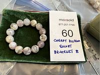 Natural cherry blossom quartz bead bracelet laid on a dark green velvet pouch with a lot tag visible.