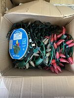 Photo of an open box containing several strands of used Christmas lights with decorative bulb covers in red and white colors.