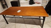 Full view of rectangular wooden coffee table with metal legs and crossbars on tiled floor.