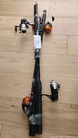 Four fishing rods with attached reels and fishing lines bundled together on a wooden floor.
