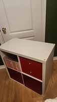 Front view of IKEA storage unit showing two red drawers on the right, pink fabric bin on upper left, and two red pull-out bins on bottom.