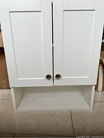Closed view of white laminated medicine cabinet with two front doors and lower open shelf.