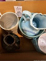 Box containing multiple ceramic pots and vases in assorted colors and styles, showing condition and variety.