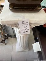 Top view of white plaster pedestal plant stand with rectangular ceramic pot on top, showing taped hole on stand surface.