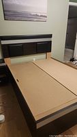 Full view of the queen size bed frame with three drawers in the base and a padded headboard with dark panels.