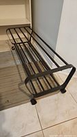 Black metal shoe rack viewed from side angle on tile floor.