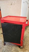 Front side view showing black lockable door, red metal body, and caster wheels underneath.