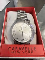 Front view of Caravelle New York men's watch in branded red box showing silver dial with Roman numeral markers.