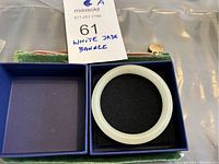 White jade bangle in a box with maxsold tag showing title.