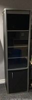 Front view of one black entertainment storage tower with glass shelves and lower cabinet door.