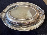 Silver serving dish with raised decorative edge and handles on black cloth