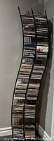 Photo shows a tall black metal CD rack filled with over 150 CDs. The rack has a curved modern design and multiple slots for holding CDs.