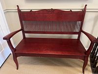 Full front view of the antique wooden hall bench showing its shape, armrests, slatted backrest, and carved wood accents.