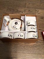 Top-down image of the boxed Japanese tea set, showing the teapot with bamboo handle and the six owl decorated teacups inside a cardboard box.