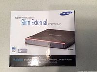 Front of the box showing Samsung SuperWriteMaster Slim External DVD Writer with model SE-S084 and compatibility with Mac and Windows.