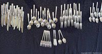 Full view of silver flatware arranged by type on black surface showing knives, forks, spoons, spreaders.