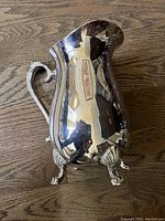 Full profile image of the sterling silver pitcher showing the overall curved body shape, decorative handle, and claw feet.