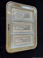 Top view of three rectangular glass dishes with decorative sunburst and textured patterns on a glass tray with compartment sections.