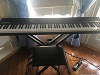 Full view of Alesis digital piano on X-style keyboard stand with piano bench chair and sustain pedal visible underneath.