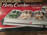 Photo of the product box showing the Betty Crocker branding and product features including three warming trays, 7.5 quart capacity, adjustable temperature, and removable lids.