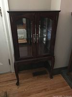 Overall view of the standing curio cabinet showing wooden frame, glass doors, and legs