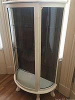 Front angled view of curio cabinet showing curved glass doors, white painted finish, and carved legs.