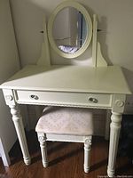 Front view of the white dressing table with oval mirror and matching padded chair underneath.