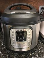 Front view of Instant Pot electric pressure cooker showing handle on lid and digital control panel.