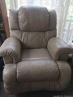Front view of beige leather recliner armchair showing padded armrests, backrest, and seat cushion with visible wear.