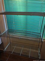 Three-tier metal rack shown stacked with three layers, placed near a window with green blinds.