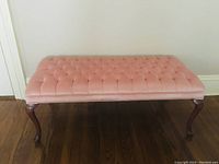 Front view of the pink tufted long chair showing upholstery and wooden legs.