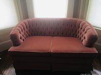 Front view of the pink velvet two-seat vintage sofa with tufted back and cushions.