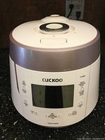 Front view of the Cuckoo pressure rice cooker showing overall shape, display screen, and control buttons.