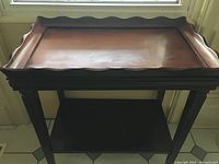 Front view of the small wooden table showcasing tray-style top with scalloped edges and open lower shelf.