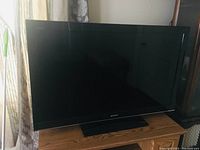 Front view of Sony Bravia TV powered off, sitting on black stand on wood surface near window.