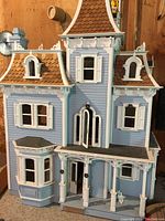 Front view of a vintage wooden dollhouse painted blue with brown roof and white trims, showing some broken parts and dust.