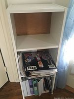 Small white bookshelf showing three shelves with various papers and binders stored on the bottom shelves.