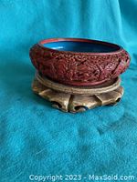 Side view of round cinnabar bowl on wooden carved base, showing dragon detail and red lacquer carving.