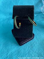 Front view of earrings displayed on black stand against turquoise backdrop