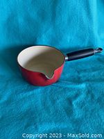 Photo of red Le Creuset pot with handle and spout against blue background showing side and interior view