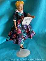 Front and side view of the Lucille Ball I Love Lucy collectible doll standing on a white base, showing floral dress and yellow molded hair.