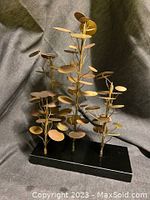 Front view of three-branched metal eucalyptus sculpture on granite base.