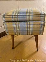 Front view showing yellow and blue plaid upholstery and walnut tapered legs of stool.