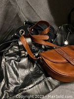Mixed bags piled together showing brown leather bag and partially visible black bags.
