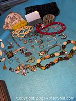Overview of mixed costume jewelry items laid out on blue cloth including necklaces, bracelets, rings, pins, and watches