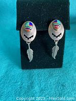 Front view of the Navajo sterling silver earrings with colorful turquoise and other stones inlay and feather dangles on a black display.